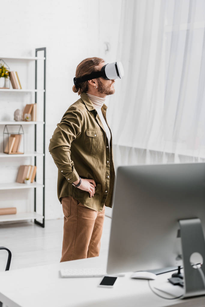 Side view of 3d artist using vr headset near table with gadgets in office  - Photo, Image