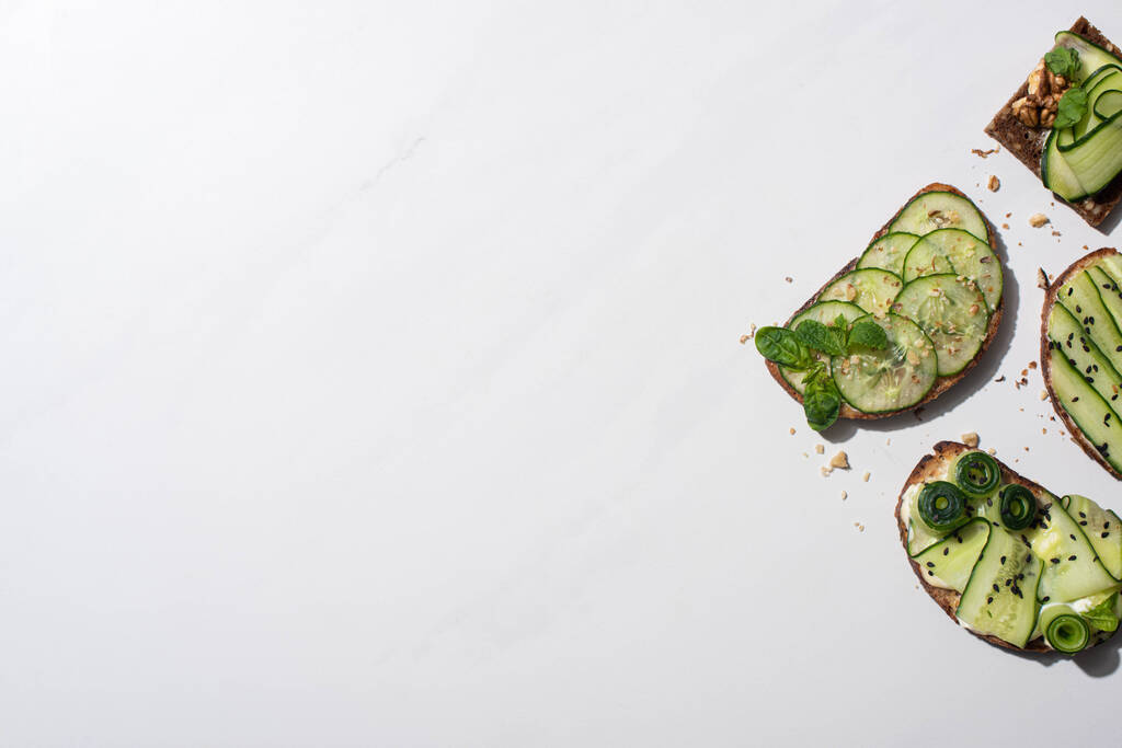 top view friss uborka pirítós magvak, menta és bazsalikom levelek fehér alapon - Fotó, kép
