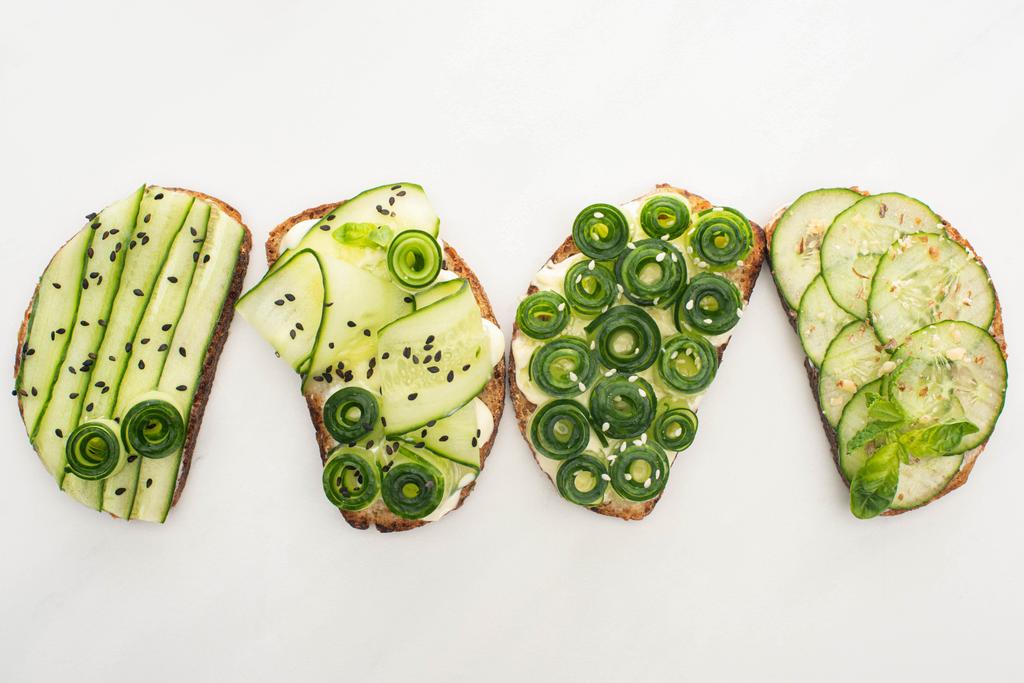 bovenaanzicht van verse komkommer toast met zaden, munt en basilicum bladeren op witte achtergrond - Foto, afbeelding