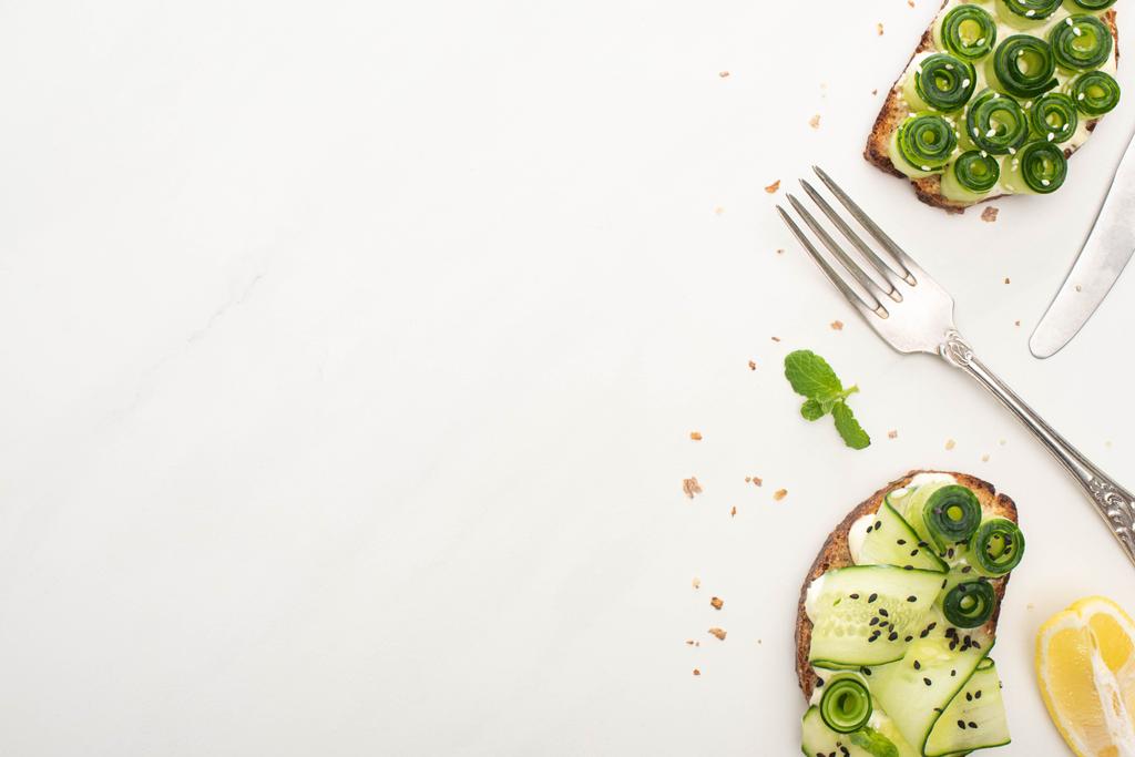 top view of fresh cucumber toasts with seeds, basil leaves and cutlery on white background - Photo, Image