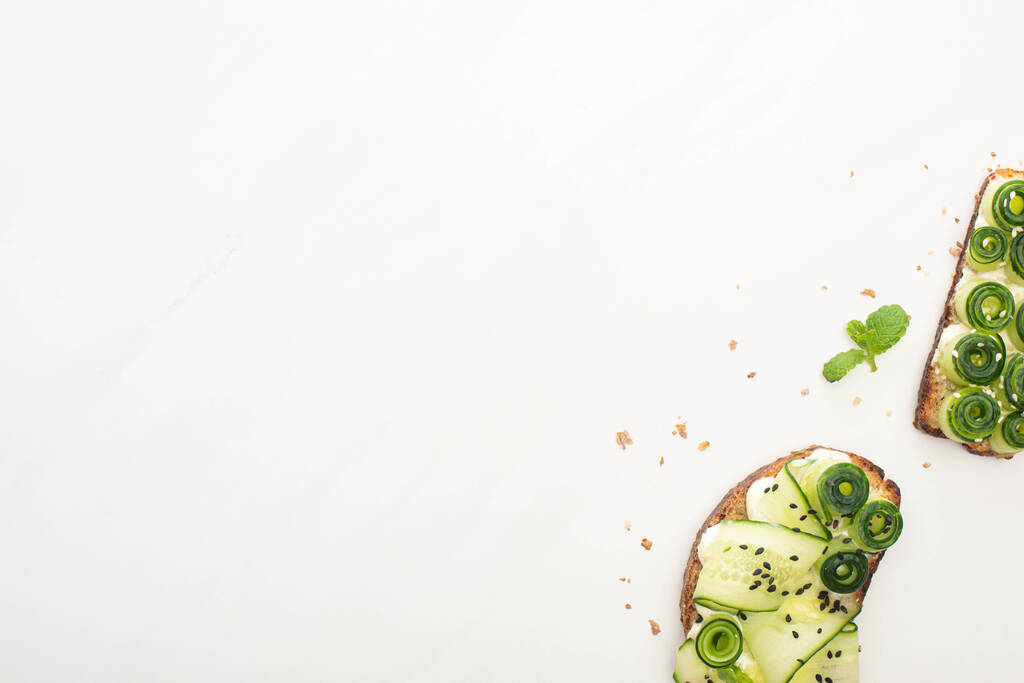 bovenaanzicht van verse komkommer toast met zaden, munt op witte achtergrond - Foto, afbeelding