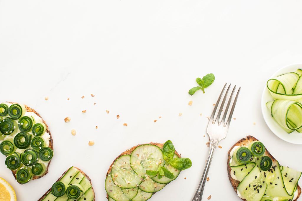 top view of fresh cucumber toasts with seeds, mint and basil leaves and fork on white background - Photo, Image