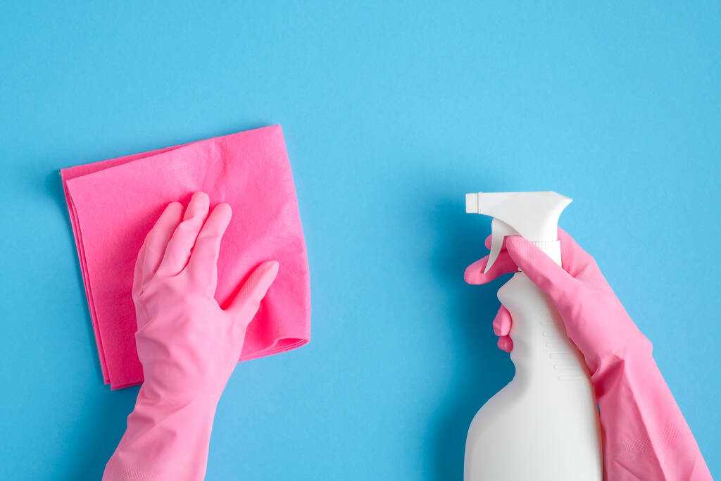 Ręce kobiet w różowych rękawiczkach z butelką sprayu do czyszczenia i serwetką sanitarną na niebieskim tle. Koncepcja sprzątania domu lub sprzątania - Zdjęcie, obraz