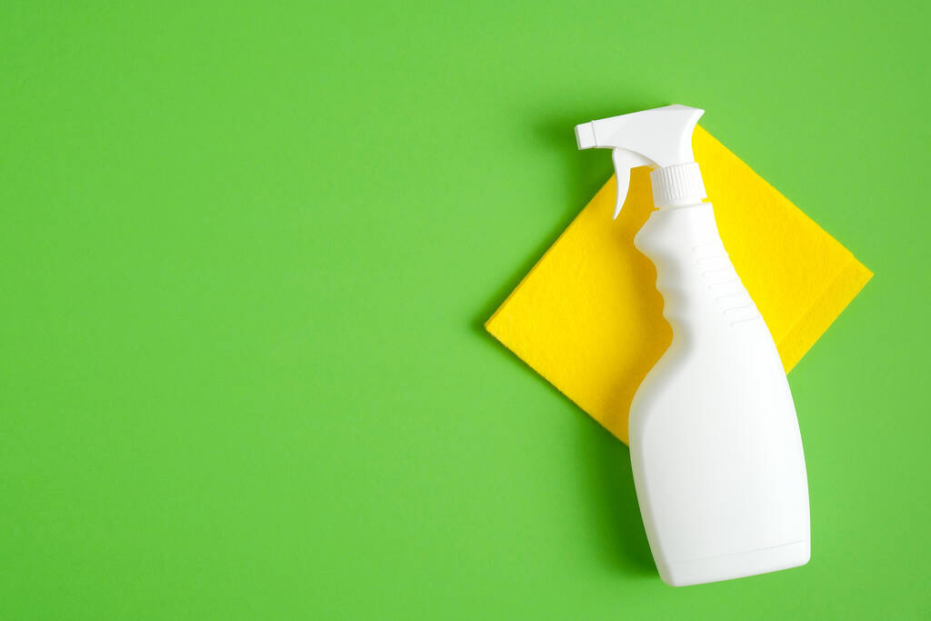 Reinigungssprayflasche auf gelber Serviette über grünem Hintergrund. Flache Lage, Draufsicht. Reinigungsdienstleistungskonzept. - Foto, Bild