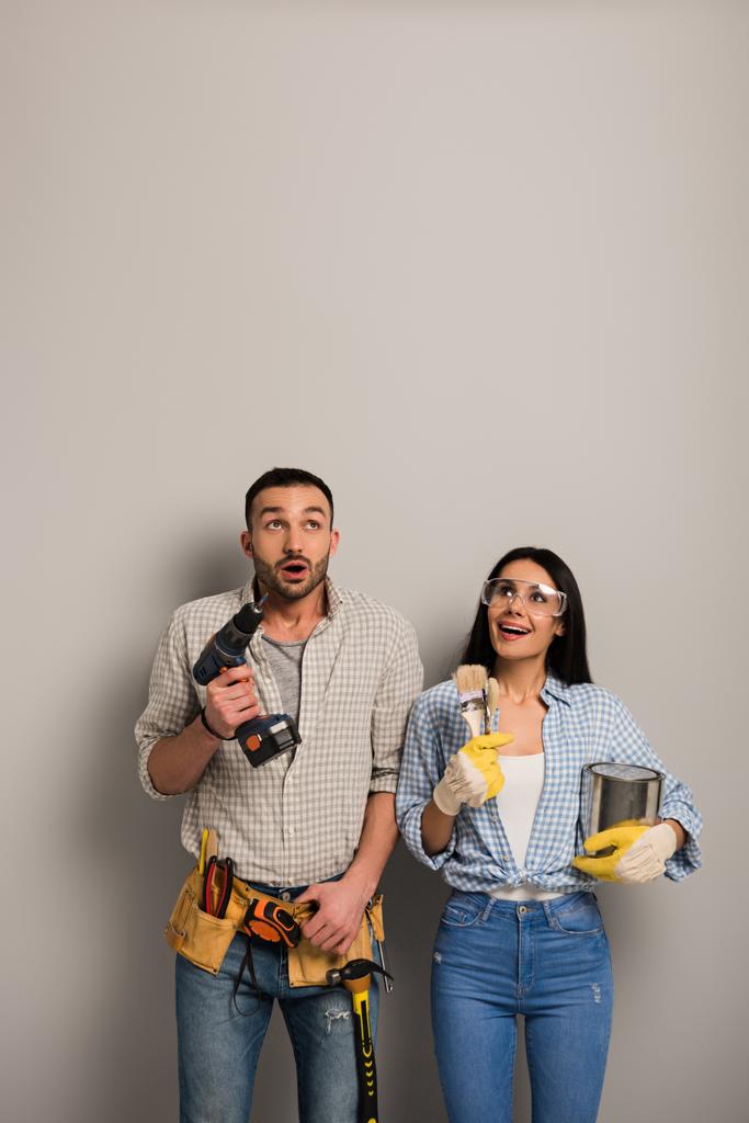 excited manual workers holding paint can, brushes and electric drill on grey  - Photo, Image