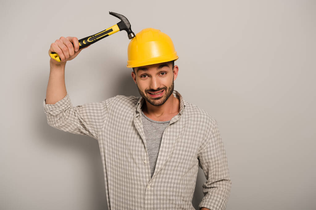 confused repairman in helmet holding hammer on grey   - Photo, Image