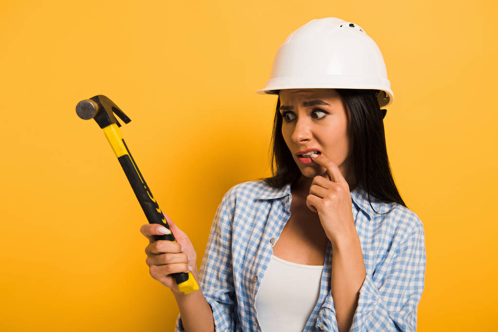 vystrašená žena ruční dělnice v helmě drží kladivo na žluté  - Fotografie, Obrázek