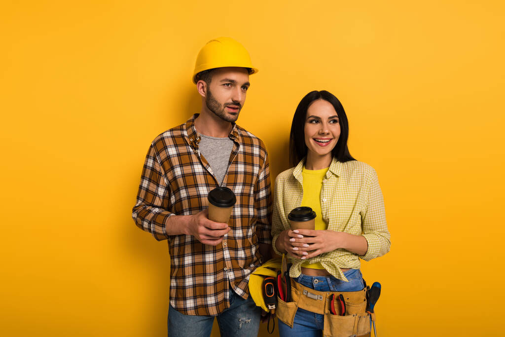 χαμογελαστοί χειρωνακτικοί εργαζόμενοι κρατώντας καφέ για να πάει στο κίτρινο      - Φωτογραφία, εικόνα