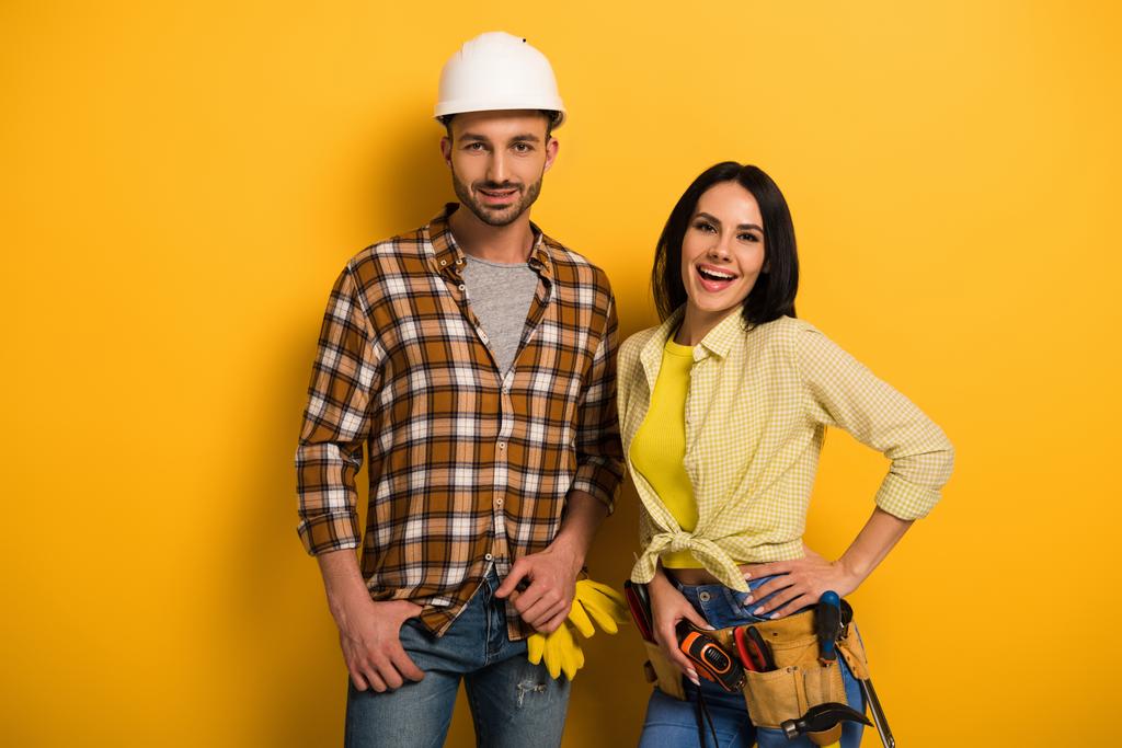 profesjonalni, uśmiechnięci pracownicy fizyczni z paskiem narzędziowym na żółto      - Zdjęcie, obraz