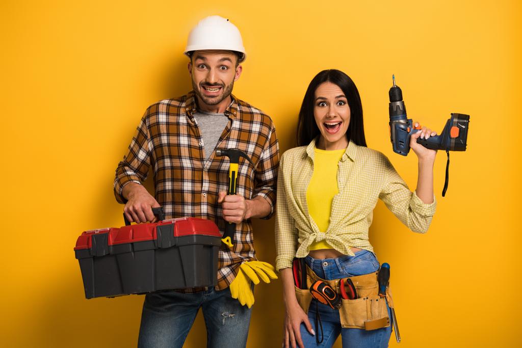 aufgeregte Heimwerkerin und Heimwerker mit Werkzeugkiste und Elektrobohrmaschine auf gelb    - Foto, Bild