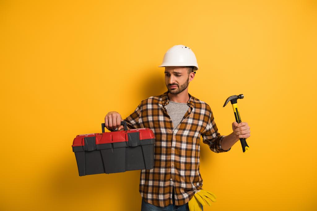 sfrustrowany pracownik fizyczny w skrzynce z narzędziami i młotkiem na żółto  - Zdjęcie, obraz
