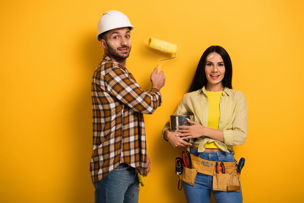 trabajadores manuales sonrientes con rodillo de pintura y lata de pintura en amarillo
   - Foto, imagen