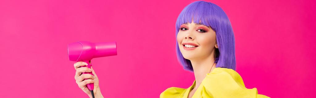 Panoramaaufnahme eines fröhlichen Pop-Art-Mädchens in lila Perücke mit Föhn, isoliert auf rosa - Foto, Bild