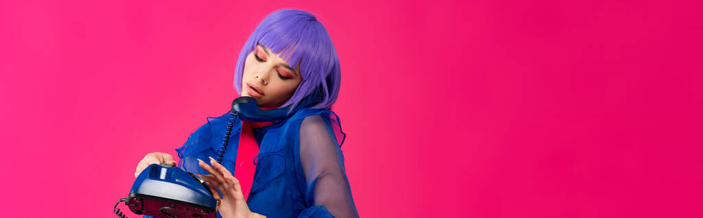 panoramic shot of beautiful trendy girl in purple wig talking on retro phone, isolated on pink - Photo, Image