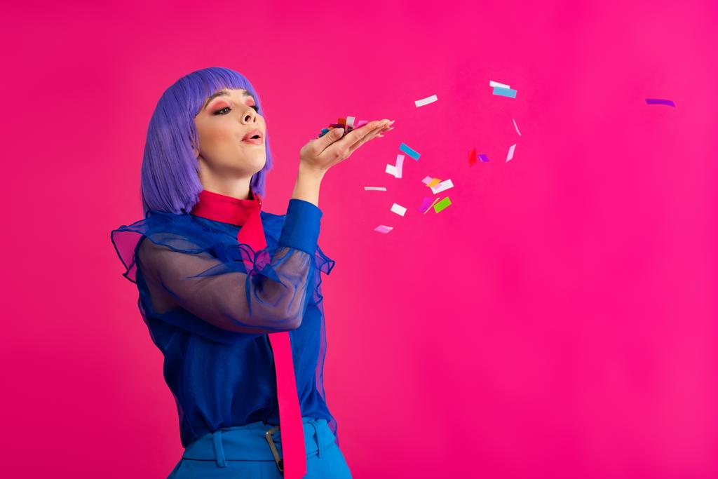 beautiful fashionable pop art girl in purple wig blowing confetti, isolated on pink - Photo, Image