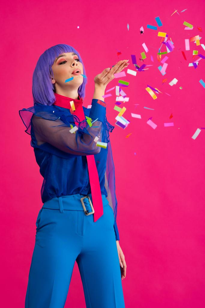 Mor peruklu çekici pop sanatçısı kız konfeti üflüyor, pembe üzerine izole edilmiş. - Fotoğraf, Görsel