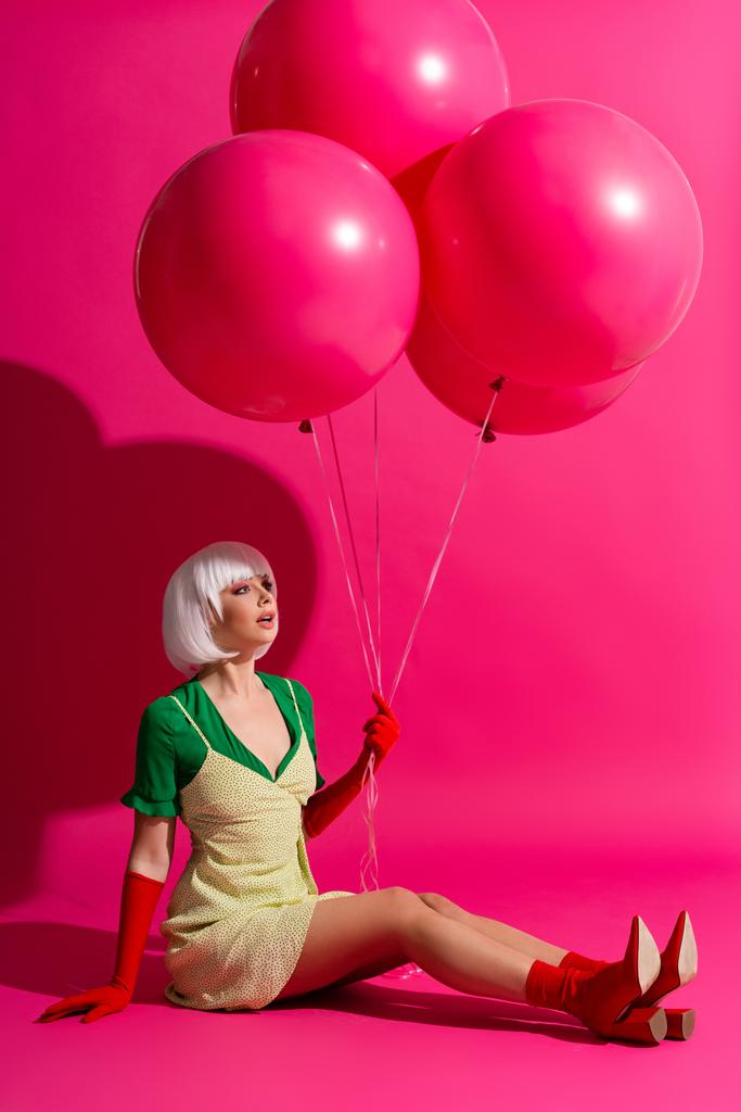 όμορφο σοκαρισμένο κορίτσι σε λευκό περούκα κρατώντας μπαλόνια σε ροζ - Φωτογραφία, εικόνα