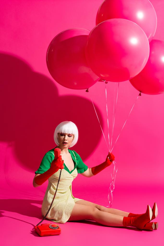 σοκαρισμένη ποπ τέχνη κορίτσι σε λευκό περούκα με μπαλόνια κοιτάζοντας vintage τηλέφωνο, σε ροζ - Φωτογραφία, εικόνα