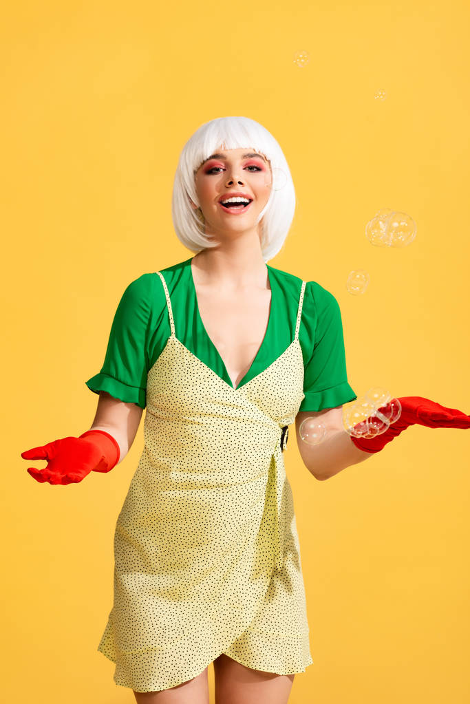 attractive happy pop art girl in white wig with soap bubbles, on yellow  - Photo, Image