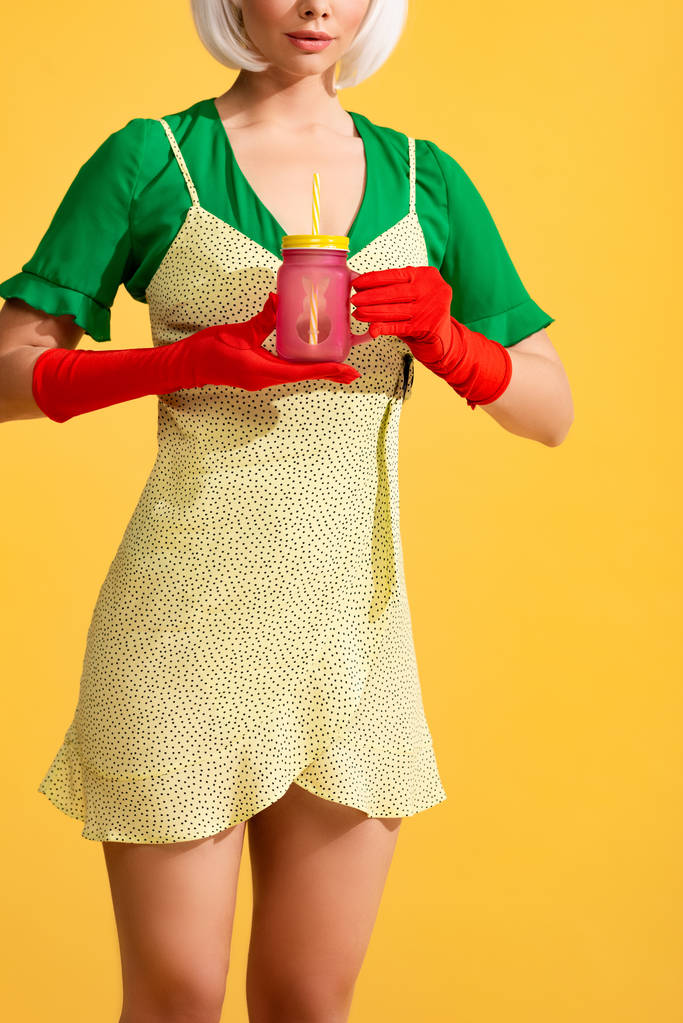 vista cortada da menina na moda em frasco vestido amarelo segurando com bebida fresca, isolado no amarelo
 - Foto, Imagem