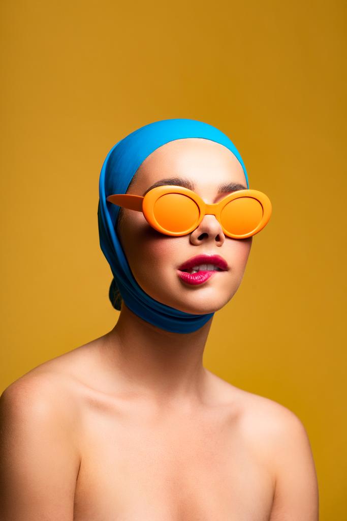 модна гола дівчина в шарфі і помаранчевих сонцезахисних окулярах кусає губу, на жовтому
 - Фото, зображення