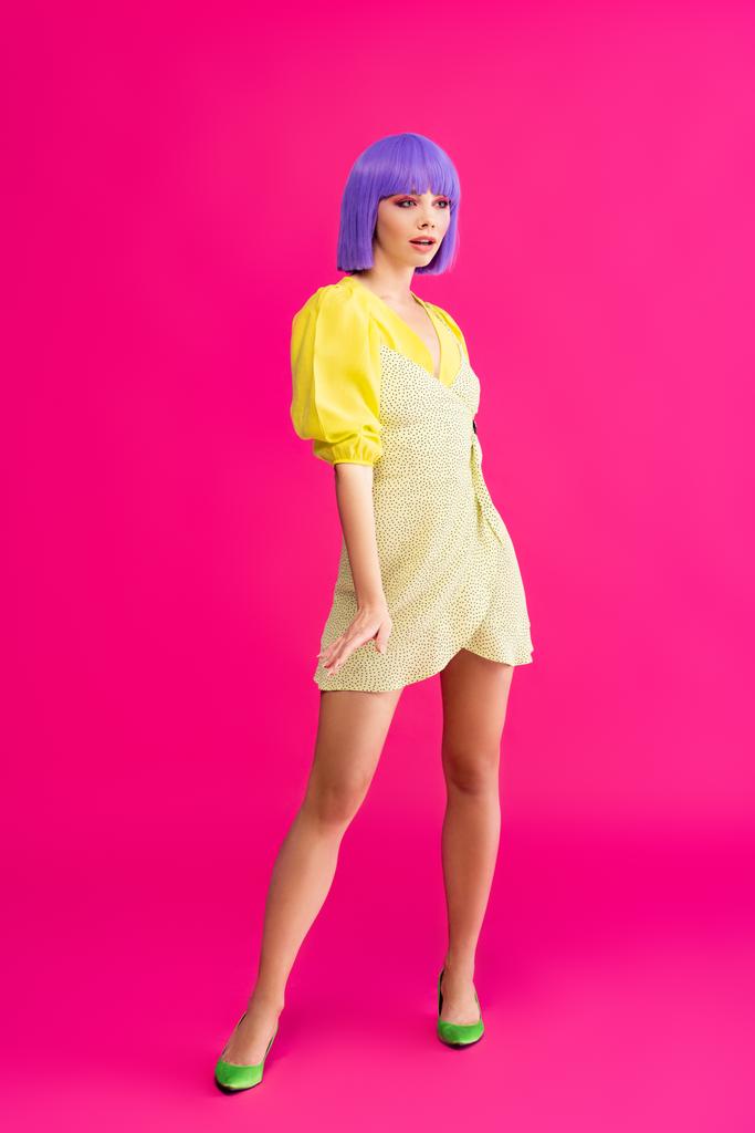 stylish pop art girl in purple wig and yellow dress posing on pink - Photo, Image