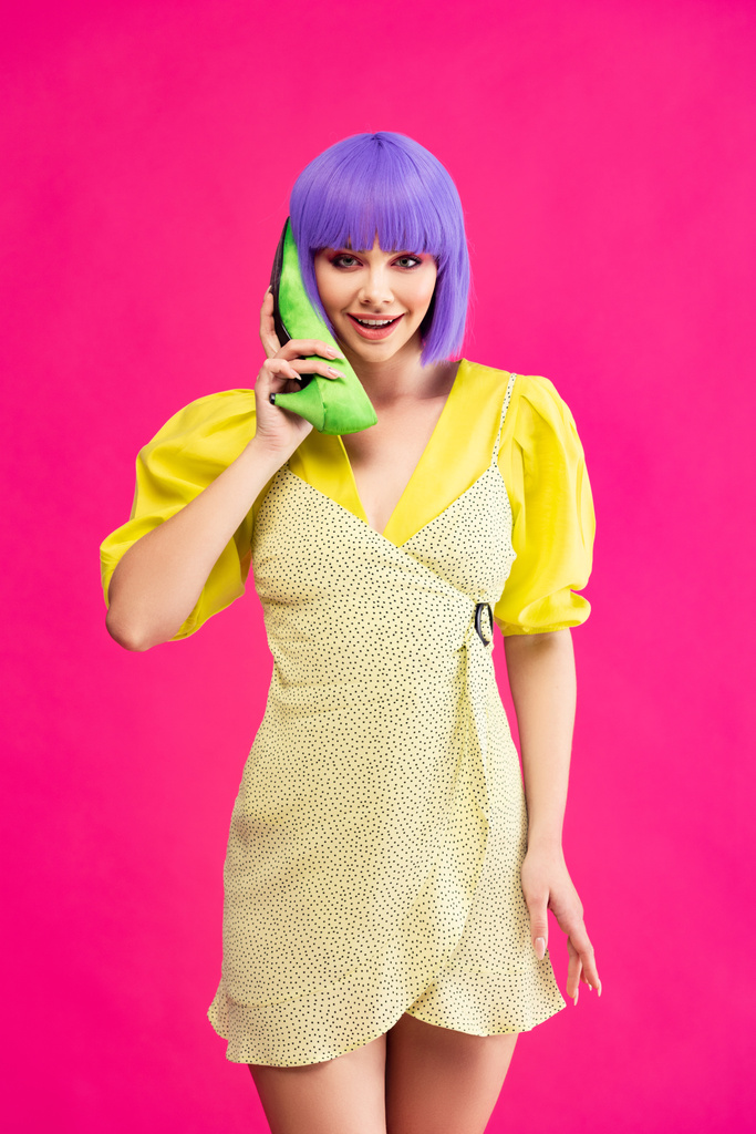 szczęśliwy pop art dziewczyna w fioletowy peruka gospodarstwa zielony but jako telefon, izolowane na różowy - Zdjęcie, obraz