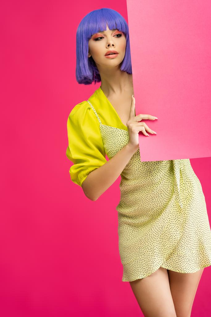 beautiful girl in purple wig and yellow dress holding blank placard, isolated on pink - Photo, Image