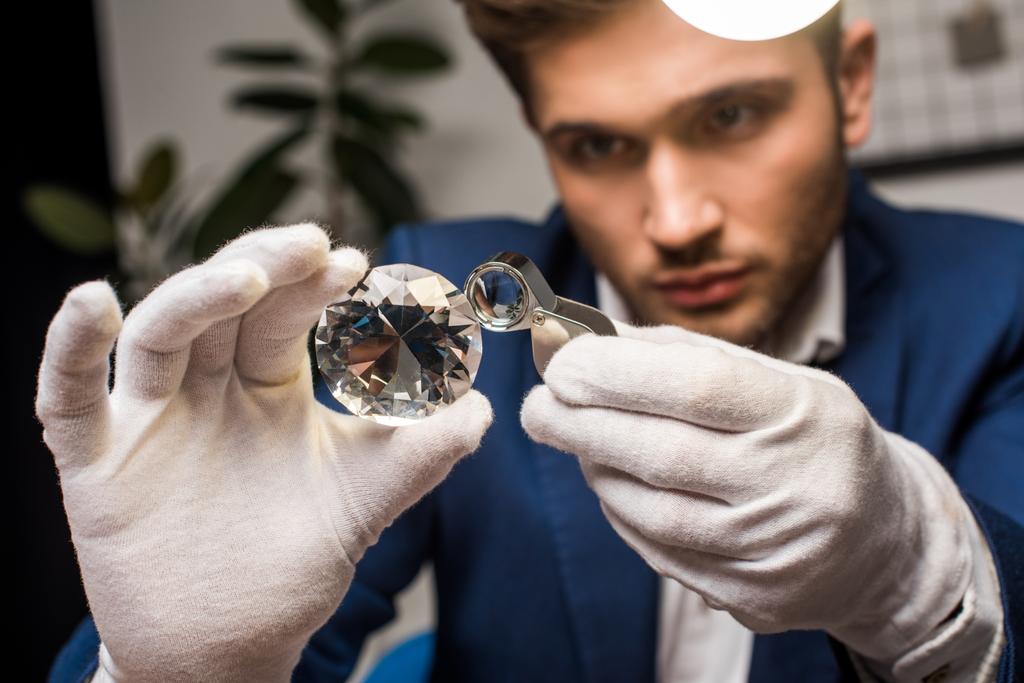 Selectieve focus van sieraden taxateur in handschoenen onderzoeken edelsteen met vergrootglas in de werkplaats - Foto, afbeelding