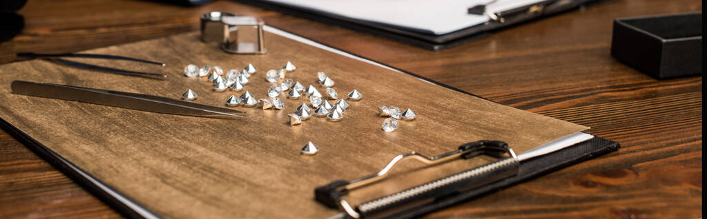 Панорамний знімок пінцетів, збільшення скла та дорогоцінних каменів на дошці на дерев'яному столі
 - Фото, зображення