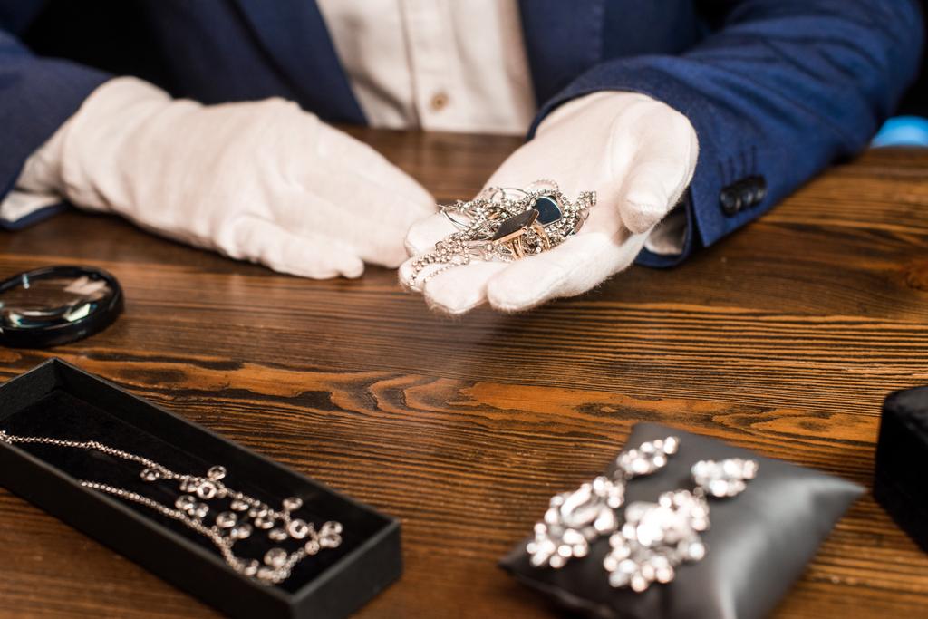 黒の背景にテーブルの上に虫眼鏡の近くに宝石を保持しているジュエリー鑑定人の作物ビュー - 写真・画像