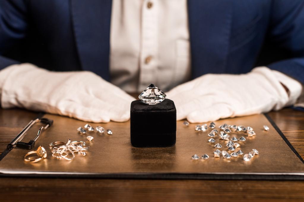 Vista cortada de pedra preciosa perto de jóias a bordo e avaliador de jóias na mesa isolada em preto
  - Foto, Imagem