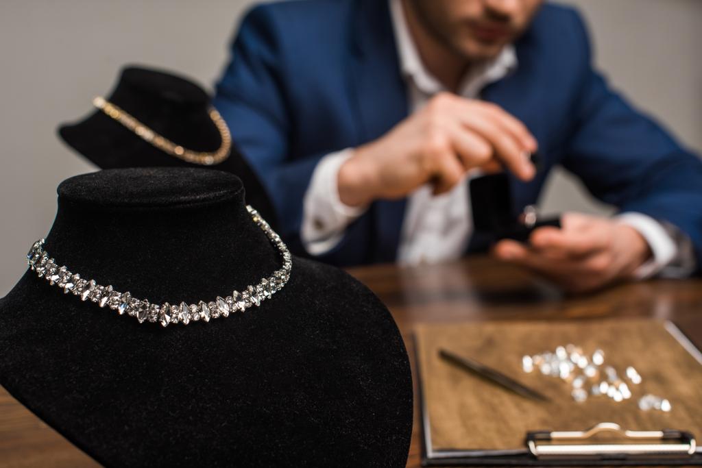 Επιλεκτική εστίαση των κολιέ σε περίπτερα κολιέ και κοσμήματα εκτιμητή εργασίας στο τραπέζι απομονώνονται σε γκρι - Φωτογραφία, εικόνα
