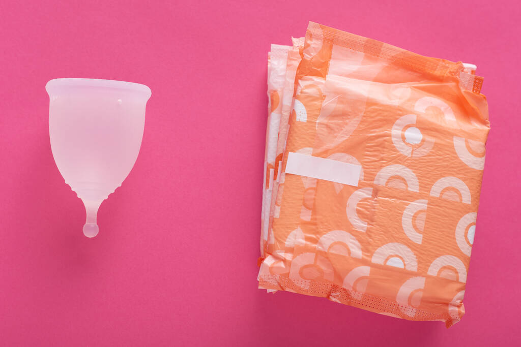 Horizontales Bild von Menstruationstasse und Hygienepolstern, die vor rosa Hintergrund isoliert werden, Auswahl für Frauen während der Menstruation, null Verschwendung von Lebensstil gegen Konsum. Flache Lagezusammensetzung. - Foto, Bild