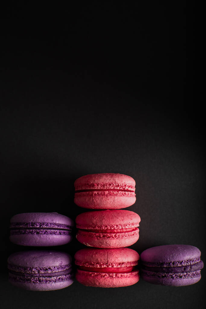 Macarrones rosados y morados sobre un fondo oscuro. Día Internacional de la Mujer. Cocina nacional francesa. Comida disparada. primer plano
 - Foto, Imagen