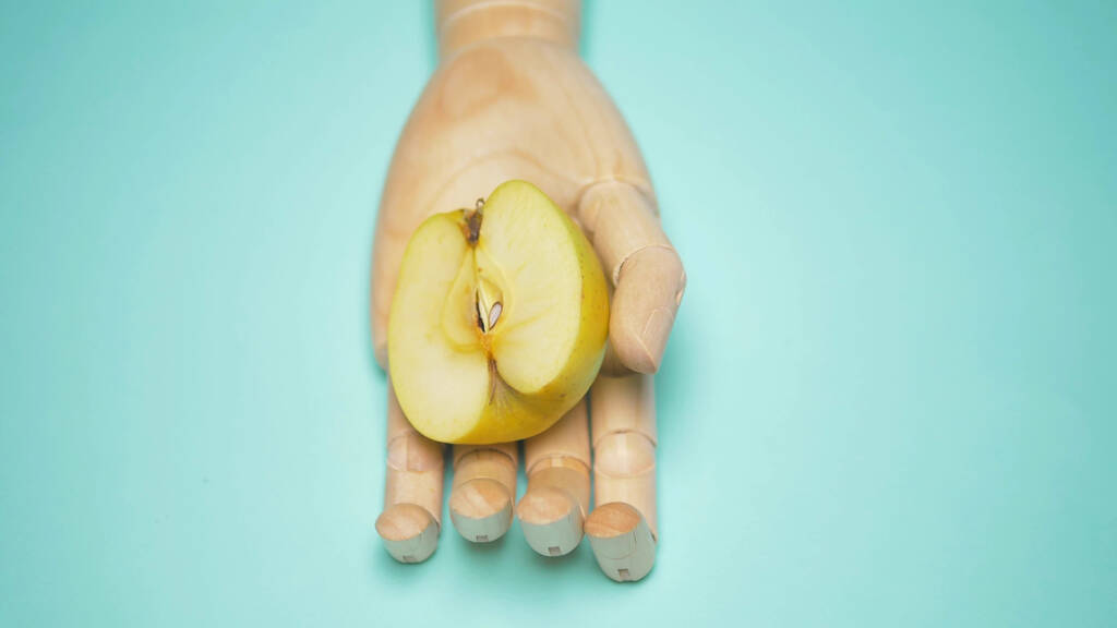 wooden hand holding half a green Apple, blue background - Photo, Image