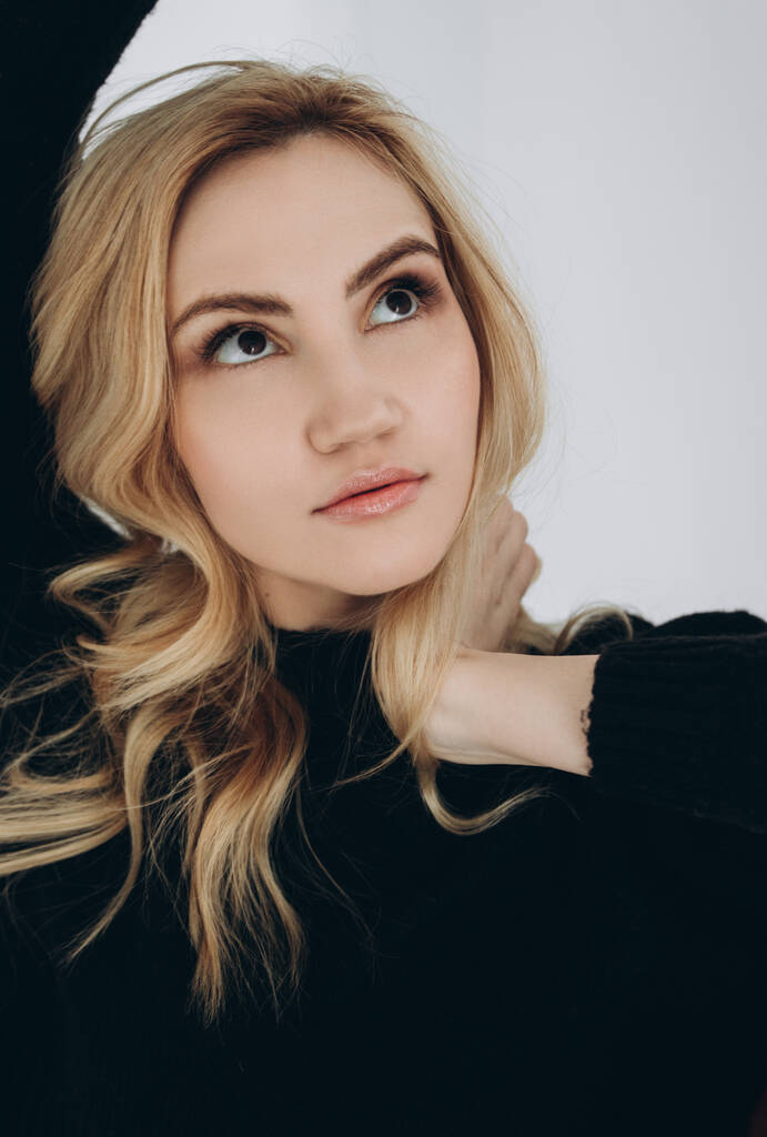 Portrait of a beautiful blonde girl with dark eyes in a black sweater. - Photo, Image