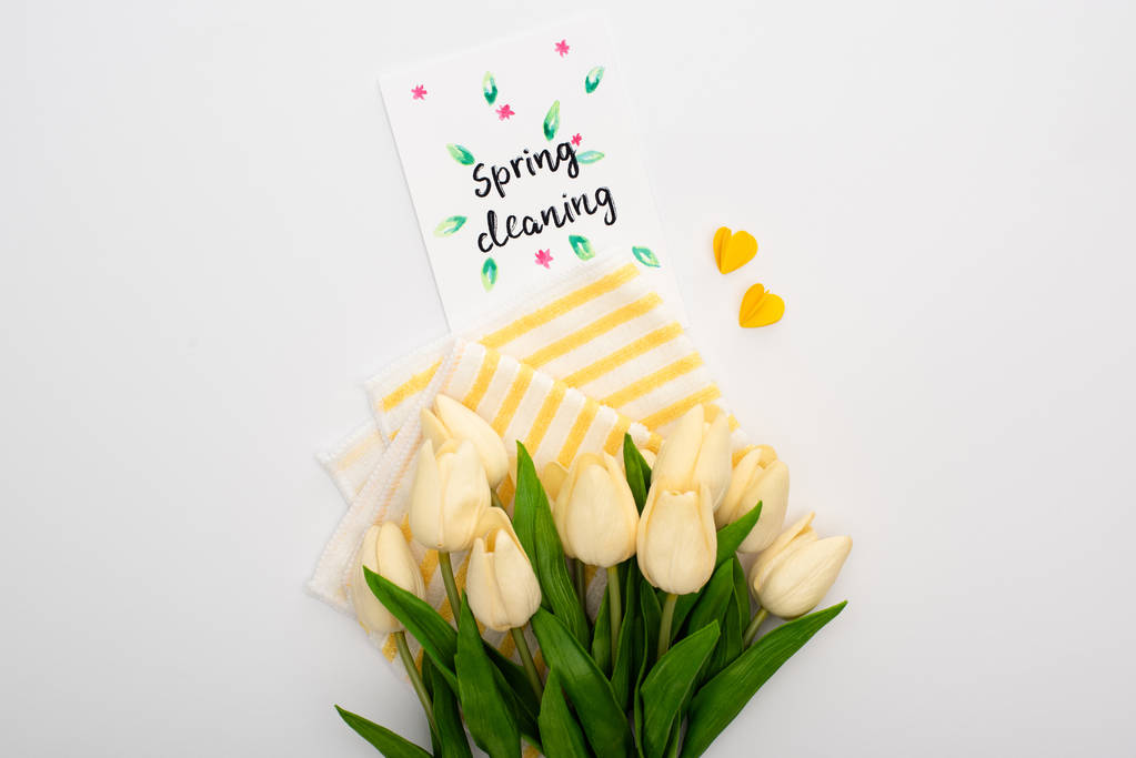 vista superior de los tulipanes de primavera y artículos de limpieza amarillos cerca de la tarjeta de limpieza de primavera sobre fondo blanco
 - Foto, Imagen