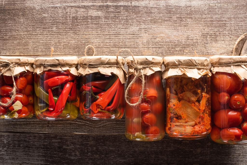 top view of red homemade tasty pickles in jars on wooden table - Photo, Image