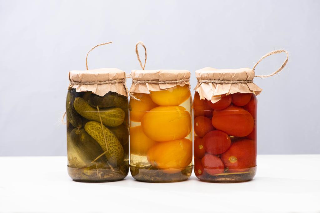 hausgemachte köstliche eingelegte Tomaten und Gurken in Gläsern isoliert auf grau - Foto, Bild