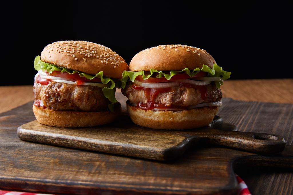 twee smakelijke hamburgers op houten snijplanken geïsoleerd op zwart - Foto, afbeelding