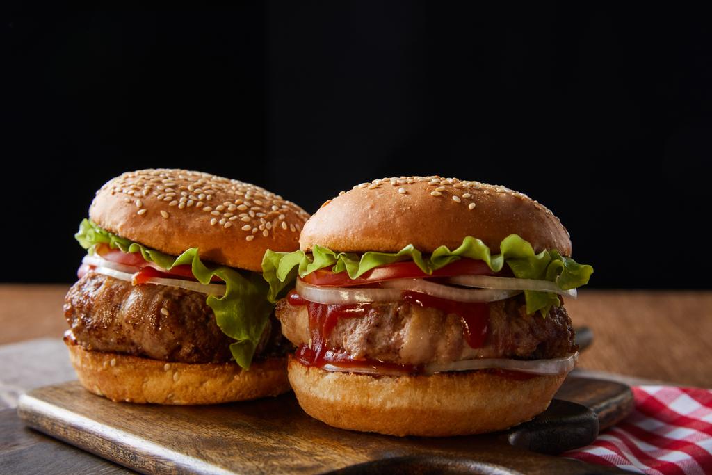 dva hamburgery na dřevěných řezacích deskách izolovaných na černé - Fotografie, Obrázek