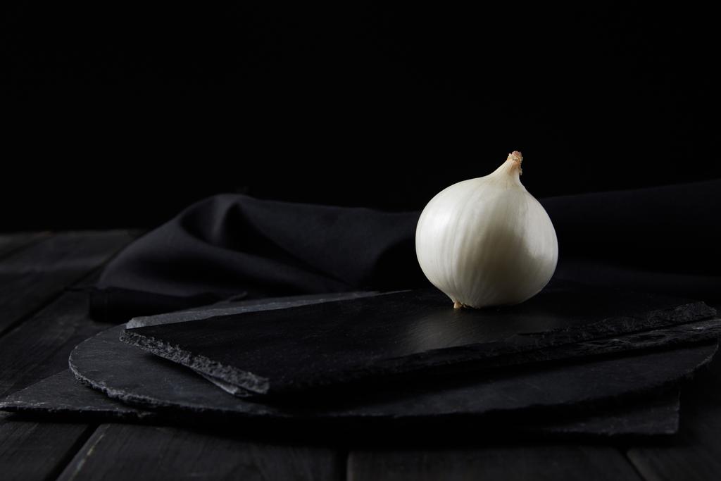 Ολόκληρο λευκό κρεμμύδι σε μαύρο ξύλο κοπής απομονωμένο σε μαύρο  - Φωτογραφία, εικόνα