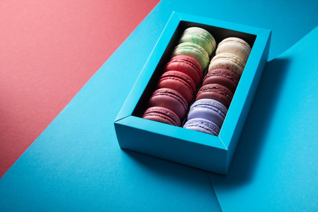 разнообразные вкусные укушенные красочные французские макароны в коробке на синем и красном фоне
 - Фото, изображение