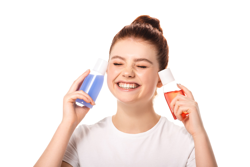emotional teenager holding two bottles with red and blue makeup removers, isolated on white - Photo, Image