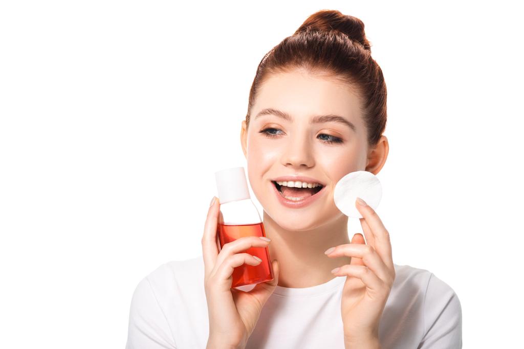excitada adolescente con piel limpia sosteniendo esponja de algodón y botella con removedor de maquillaje rojo, aislado en blanco
 - Foto, imagen