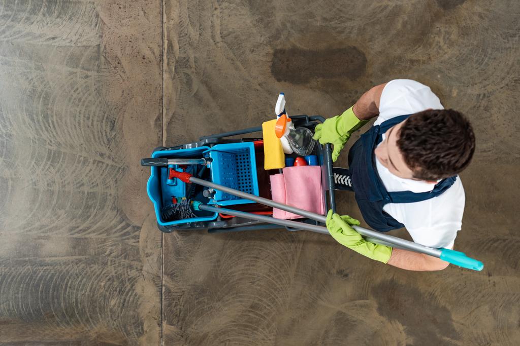 top view of cleaner in uniform carrying cart with cleaning supplies - Photo, Image