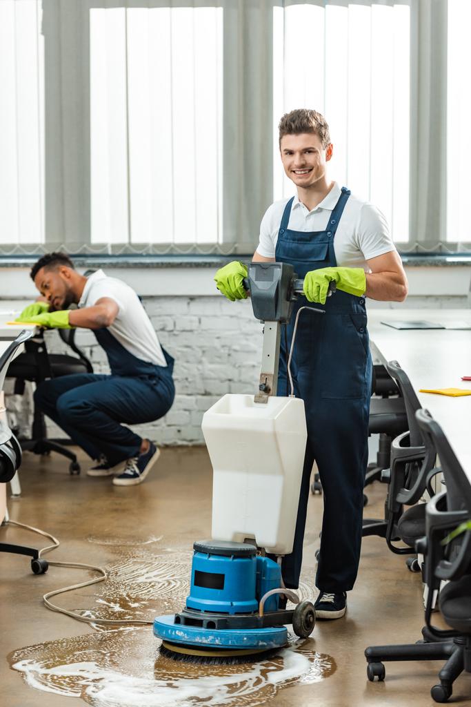 šťastný čistič praní podlahy s čistícím strojem, zatímco kolega otírání stolu - Fotografie, Obrázek