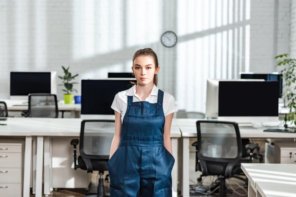 serious young cleaner in overalls looking at camera while holding hands in pockets - Photo, Image