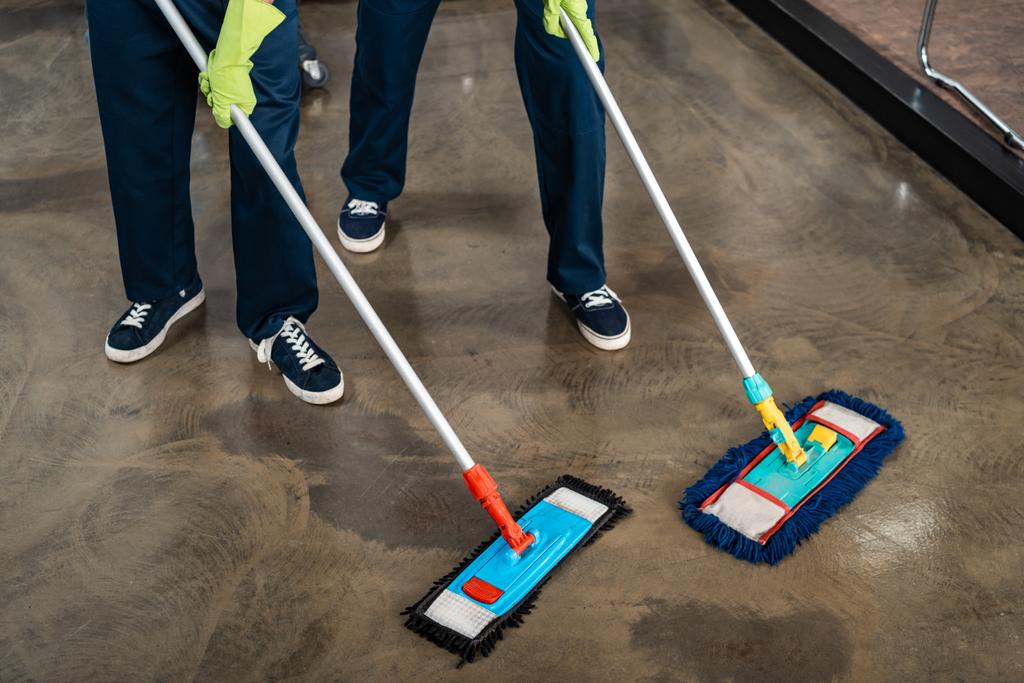 vista recortada de dos limpiadores lavando piso con trapeadores
 - Foto, Imagen